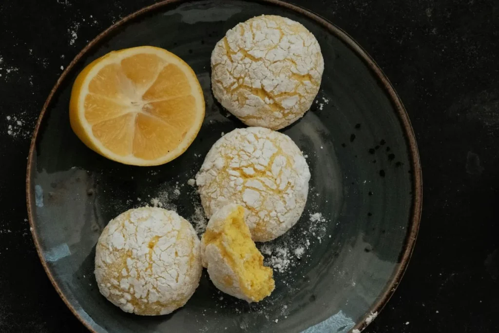 Biscotti crinkle al limone e zucchero a velo con fette di limone fresco, ideali con olio EVO delicato.